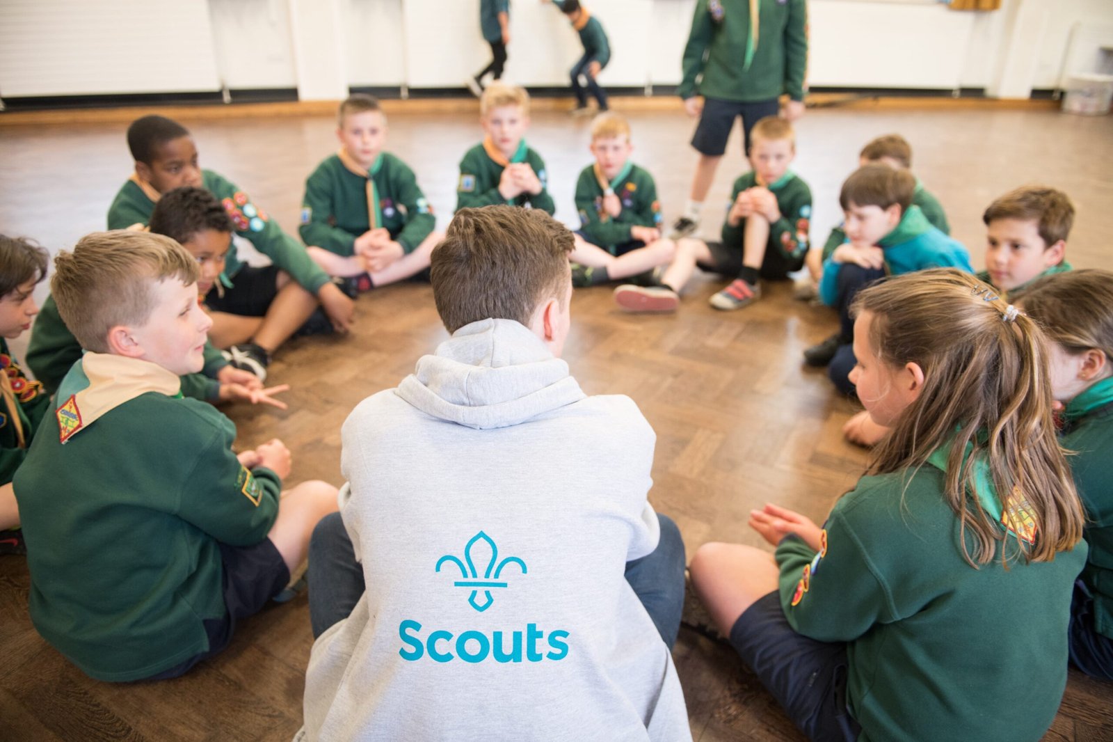 A man sat in a circle with a group of Cub Scouts. 